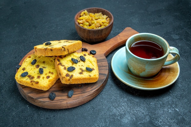 Vorderansicht köstliche Rosinenkuchen mit frischen Rosinen und einer Tasse Tee auf dunklem Raum