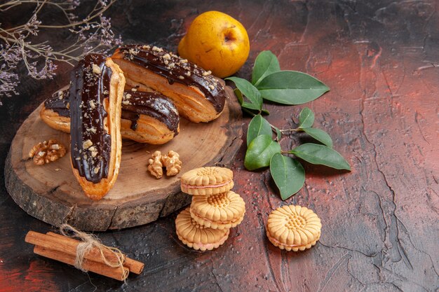 Vorderansicht köstliche Schoko-Eclairs mit Keksen auf dunklem Hintergrund