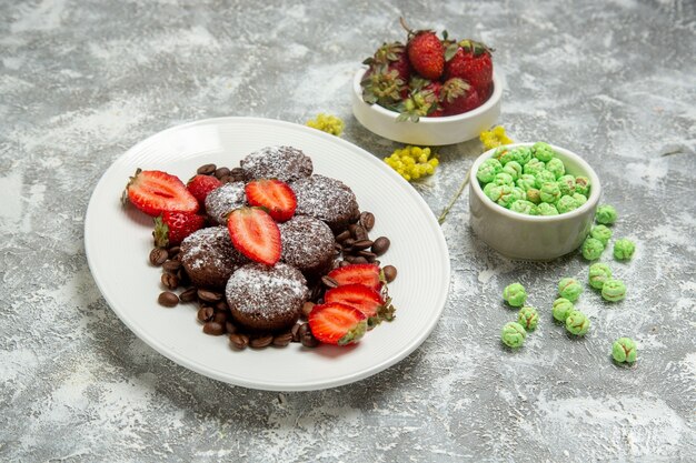 Vorderansicht köstliche Schokoladenkuchen mit Bonbons und Erdbeeren auf weißer Oberfläche Kekszuckerkuchen süßer Tee-Keks