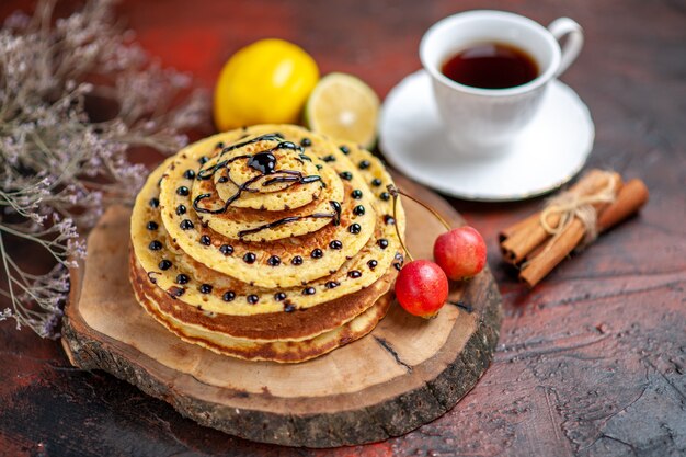 Vorderansicht köstliche süße Pfannkuchen mit Tasse Tee auf dem dunklen Hintergrund