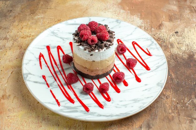 Vorderansicht köstlicher cremiger Kuchen im Teller mit Himbeeren auf braunem Tisch