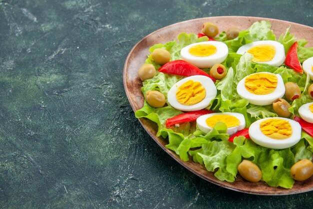 Vorderansicht köstlicher Eiersalat mit grünem Salat und Oliven auf dunkelblauem Hintergrund