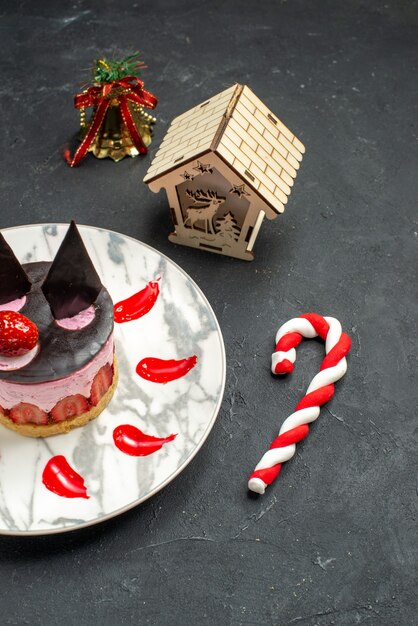Vorderansicht köstlicher Käsekuchen mit Erdbeere und Schokolade auf ovalem Teller Weihnachtsbaumspielzeug auf dunkel