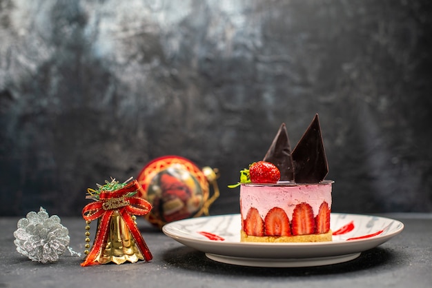 Vorderansicht köstlicher Käsekuchen mit Erdbeere und Schokolade auf ovalem Teller Weihnachtsbaumspielzeug auf dunklem Freiraum
