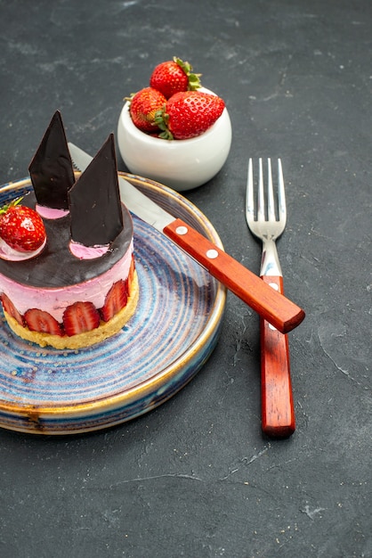 Vorderansicht köstlicher Käsekuchen mit Erdbeere und Schokolade ein Messer auf einer Tellerschüssel mit Erdbeeren eine Gabel auf dunkel