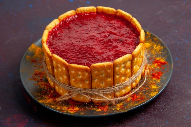 Kostenloses Foto vorderansicht köstlicher kuchen mit roter sahne und crackerplätzchen auf der dunklen oberfläche kekskuchenzuckerdesserttorte süße kekse