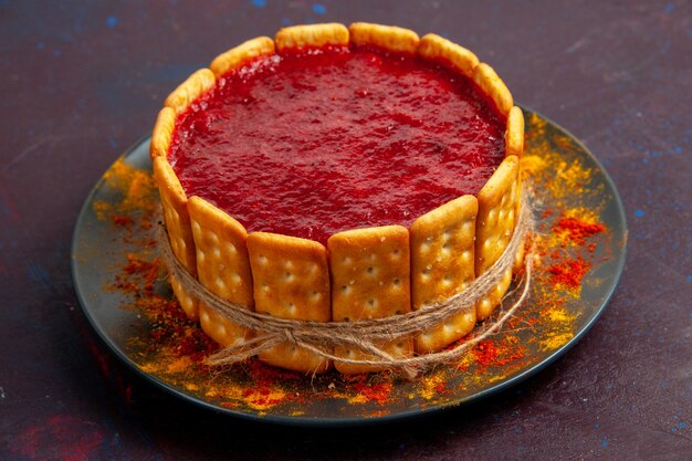 Vorderansicht köstlicher Kuchen mit roter Sahne und Crackerplätzchen auf der dunklen Oberfläche Kekskuchenzuckerdesserttorte süße Kekse