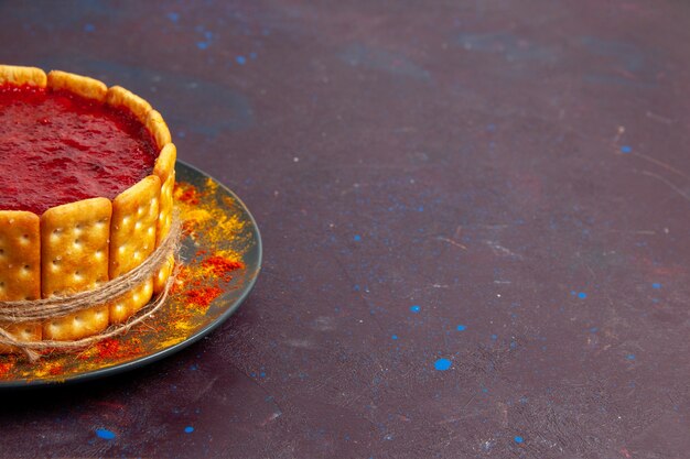 Vorderansicht köstlicher Kuchen mit roter Sahne und Crackerplätzchen auf dunklem Kekskuchen-Zuckerdessertkuchen süßer Keks