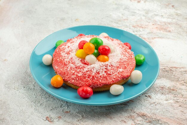 Vorderansicht köstlicher rosa Kuchen mit bunten Bonbons im Teller auf weißem Hintergrund Kuchen Regenbogenfarben Kuchen Dessert Süßigkeiten rainbow