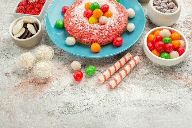 Vorderansicht köstlicher rosa Kuchen mit bunten Süßigkeiten auf weißem Schreibtisch Dessert Goodie Regenbogenfarben Kuchen Süßigkeiten