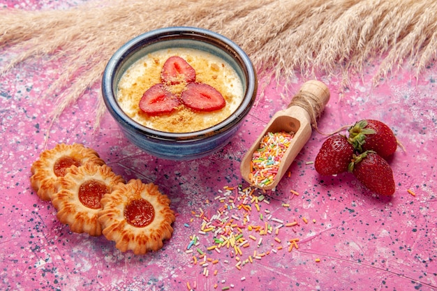 Vorderansicht köstliches cremiges Dessert mit rot geschnittenen Erdbeeren und kleinen Keksen auf hellrosa Wanddessert Eisbeerencreme süße Frucht