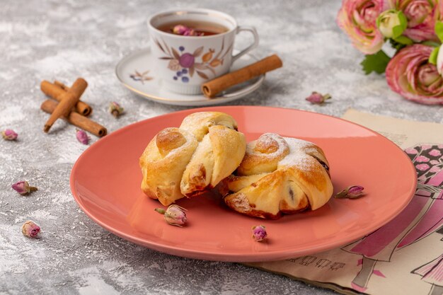 Vorderansicht köstliches Gebäck mit Füllung Innenplatte zusammen mit Tee und Zimt auf dem weißen Tisch, süßer Zuckerkuchen backen Gebäck