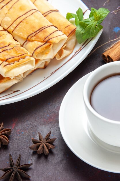 Vorderansicht köstliches süßes Gebäck mit Tasse Tee auf dunklem Raum