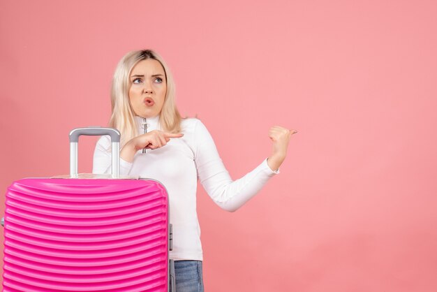 Vorderansicht koinfundierte schöne Frau mit rosa Koffer, der auf etwas zeigt