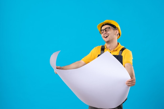 Vorderansicht lachender männlicher Baumeister in Uniform mit Papierplan auf Blau