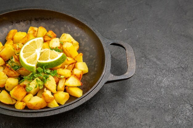 Vorderansicht leckere Bratkartoffeln in der Pfanne mit Zitronenscheiben auf dem dunklen Tisch