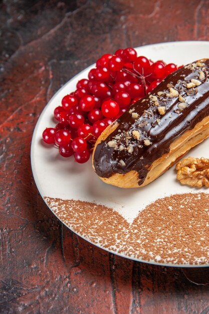 Vorderansicht leckere Choco Eclairs mit roten Beeren auf dem dunklen Tischkuchen-Dessertkuchen süß