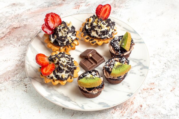 Vorderansicht leckere cremige Kuchen kleine Desserts für Tee mit Schokoladenstückchen auf weißem Hintergrund Obstkuchen Sahnekeks Kuchentee