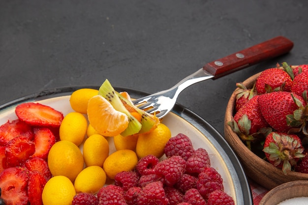 Vorderansicht leckere geschnittene Früchte mit frischen Beeren und Früchten auf dunklem, ausgereiftem exotischem tropischem Obst gesundes Leben