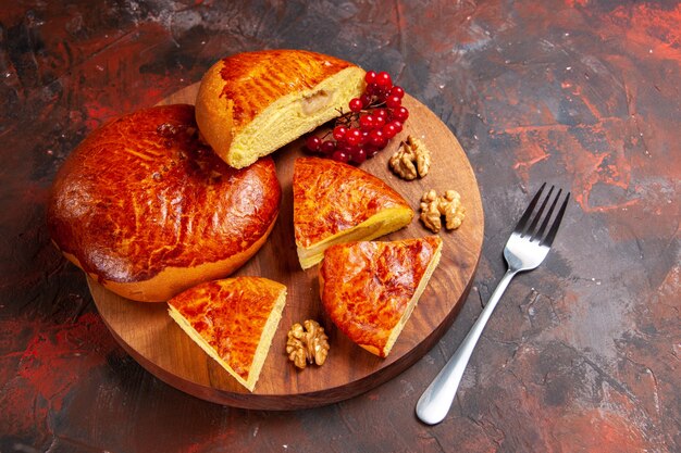 Vorderansicht leckere Kuchen geschnitten mit roten Beeren auf dunklem Schreibtisch Gebäckkuchen Kuchen süß