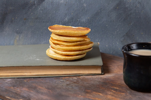 Vorderansicht leckere leckere Pfannkuchen mit schwarzer Tasse Milch auf dem grauen Hintergrund Essen Mahlzeit Frühstück