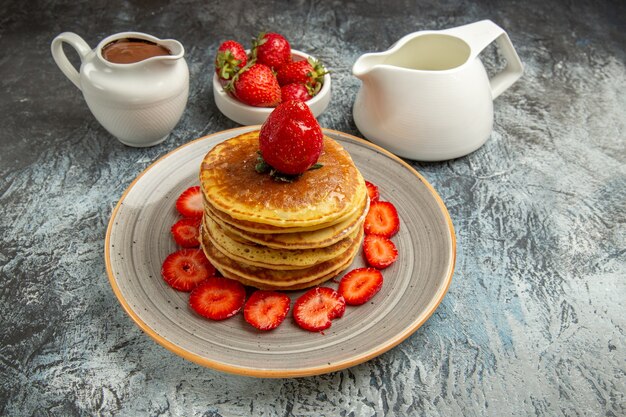 Vorderansicht leckere Pfannkuchen mit Erdbeeren und Honig auf leichtem süßem Obstkuchen der leichten Oberfläche