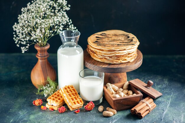 Vorderansicht leckere Pfannkuchen mit frischer Milch und Nüssen auf dunkelblauem Dessertkuchen Honigkuchen Frühstück süßer Milchmorgen