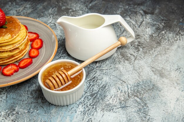 Vorderansicht leckere Pfannkuchen mit Früchten und Honig auf leichter Oberfläche Obstkuchen süß