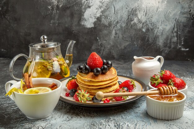 Vorderansicht leckere Pfannkuchen mit Früchten und Tee auf leichtem Oberflächenfruchtfruchtfrühstück