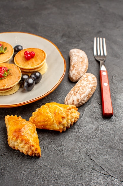 Vorderansicht leckere Pfannkuchen mit Kuchen und Früchten auf dunklem Obstkuchen der dunklen Oberfläche