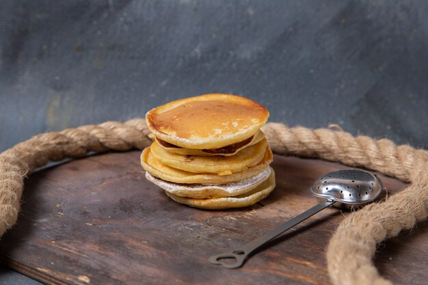 Vorderansicht leckere Pfannkuchen mit Seilen auf dem hölzernen Hintergrund süßes Zuckernahrungsmittelmahlzeitfrühstück