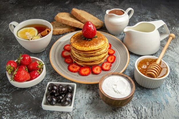 Vorderansicht leckere Pfannkuchen mit Tee und Früchten auf der leichten Oberfläche Obstkuchen süß