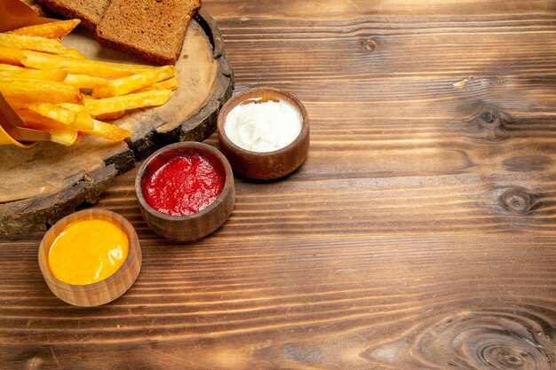 Vorderansicht leckere Pommes frites mit Gewürzen auf braunen Schreibtischkartoffeln Fast-Food-Brotmahlzeit