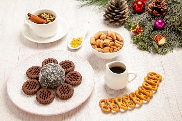 Vorderansicht leckere schokoladenkekse mit kleinem kakaokuchen und tee auf weißem schreibtisch teekuchen süßer kuchenplätzchenkeks