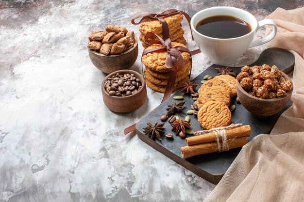 Vorderansicht leckere süße Kekse mit Kaffeesamen und Tasse Kaffee auf heller Hintergrundfarbe Kakaozuckerteeplätzchen süßer Kuchenkuchen