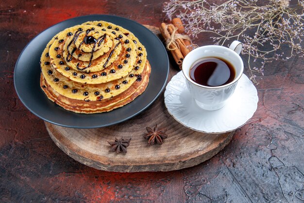 Vorderansicht leckere süße Pfannkuchen mit Tasse Tee auf dunklem Hintergrund süße Kuchen Dessert Milch