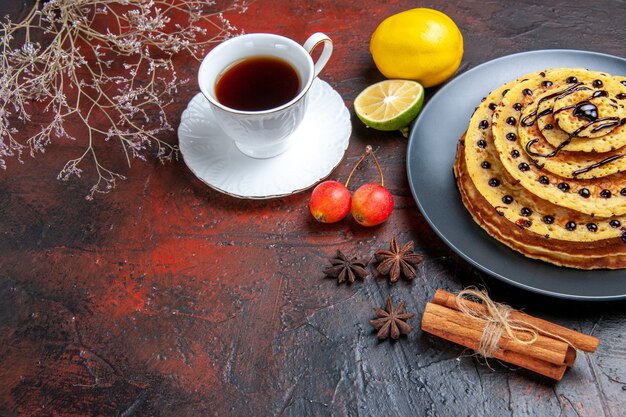 Vorderansicht leckere süße Pfannkuchen mit Tasse Tee auf dunklem Hintergrund