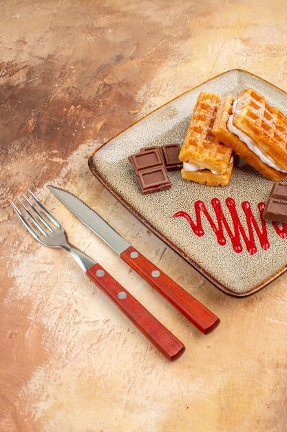 Vorderansicht leckere Waffelkuchen mit Schokoriegeln auf braunem Schreibtisch