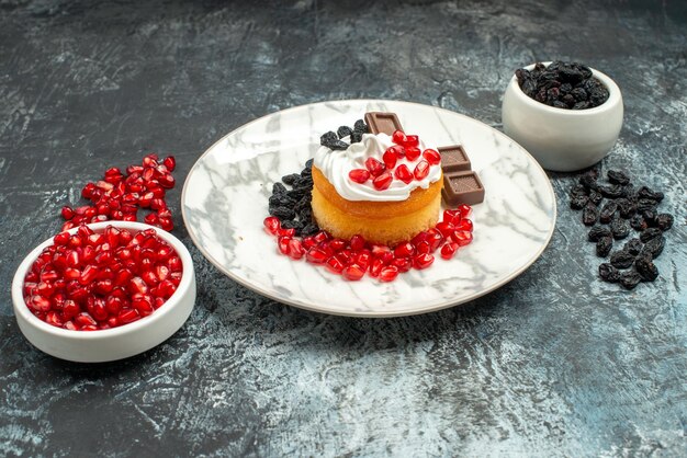 Vorderansicht leckerer cremiger Kuchen mit Schokogranatapfeln und Rosinen auf hell-dunklem Hintergrund