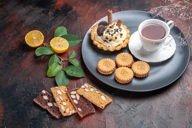 Vorderansicht leckerer cremiger Kuchen mit Tee auf dunklem Tisch süßer Kuchen Nachtisch