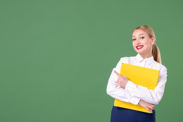 Vorderansicht Lehrerin, die gelbe Dateien auf grünem Hintergrund hält Buch studieren Uniform Lektion Bibliothek Studenten Schularbeit Universitätsfrau