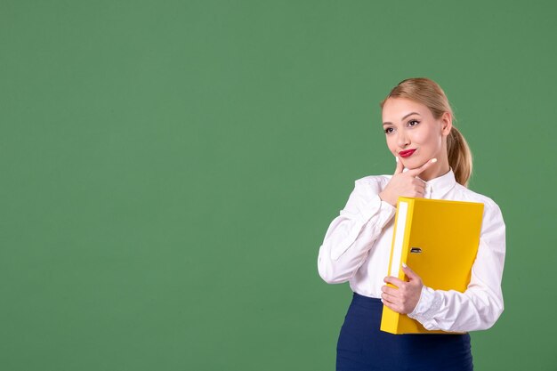 Vorderansicht Lehrerin, die gelbe Dateien auf grünem Hintergrund hält Schulunterrichtsbuch Studie Arbeit Student Universität Uniform Bibliothek