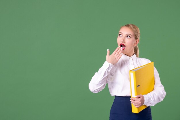 Vorderansicht Lehrerin, die gelbe Dateien auf grünem Hintergrund hält Studie Uniform Frau Universitätsbibliothek Arbeit Student Buch Schule