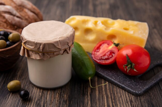 Vorderansicht Maasdam Käse mit Tomaten und Gurken auf einem Ständer mit Oliven mit Joghurt auf dem Tisch