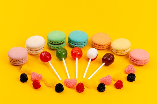 Vorderansicht Macarons und Lutscher zusammen mit Marmeladen, die auf gelben, süßen Süßigkeiten des Zuckerkuchens isoliert werden