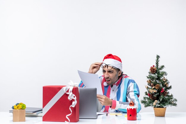 Vorderansicht männlicher Arbeiter, der an seinem Platz mit Laptop sitzt und mit Dokumenten Bürojob Emotion Weihnachten arbeitet