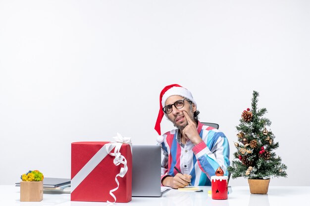 Vorderansicht männlicher Arbeiter, der an seinem Platz mit Laptop und Akten sitzt und Notizen schreibt Weihnachtsferien Bürojob