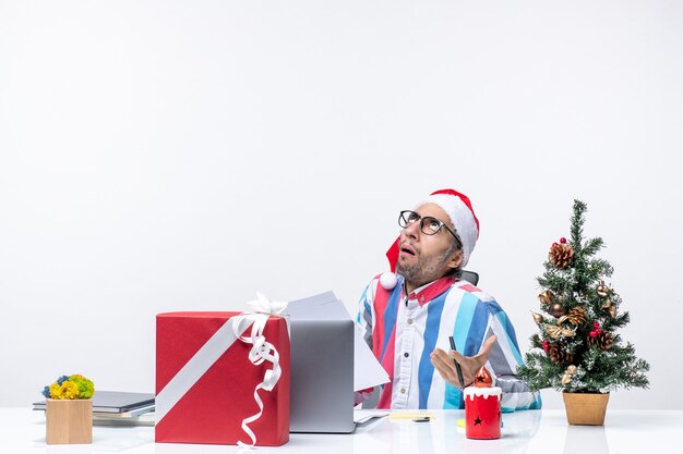 Vorderansicht männlicher Arbeiter sitzt an seinem Platz mit Laptop und Dateien, die mit Dokumenten arbeiten Büro Emotionen Job Weihnachten