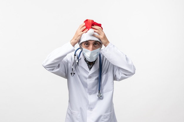Vorderansicht männlicher Arzt, der rote Kappe auf weißer Wand Neujahrs-Covid-Virus-Pandemie trägt
