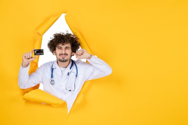 Vorderansicht männlicher Arzt im medizinischen Anzug, der eine Bankkarte auf gelber, zerrissener Farbe hält